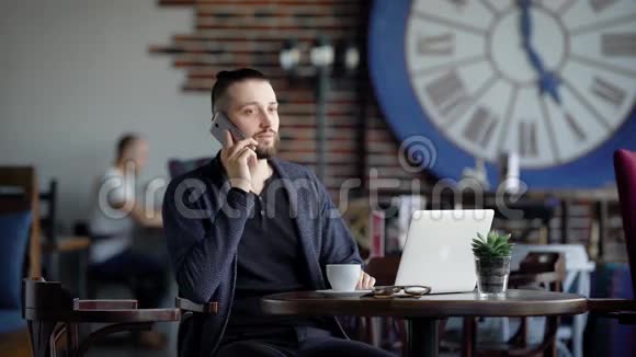 帅哥坐在餐厅的桌子旁在电话里说话时髦的年轻学生休闲视频的预览图