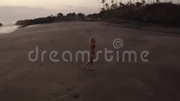 日落时分美丽的比基尼女郎在黑色海滩上的鸟瞰视频的预览图