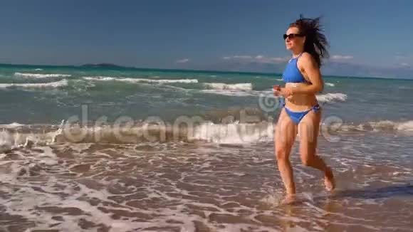 海滩比基尼女郎无忧无虑地沿着海滩上的水奔跑希腊科孚海岸风景如画缓慢的概念视频的预览图