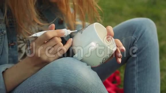 在白色杯子上特写女性的手画花图案女孩在草地上画装饰品视频的预览图