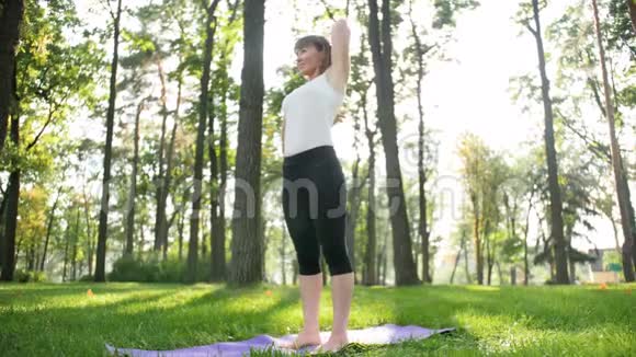 4K慢动作视频中老年微笑妇女在阳光明媚的夏日在公园练习瑜伽和冥想视频的预览图