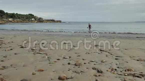 年轻女性独自一人在无人居住的野生大西洋海岸与岩石和沙子北欧风格自然环境视频的预览图