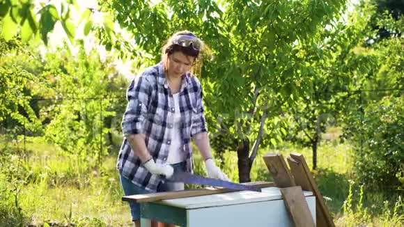 戴着防护手套的女工匠在阳光花园锯木板视频的预览图