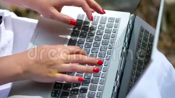 夏天户外女性手部特写用鲜红色指甲在笔记本电脑键盘上打字在笔记本电脑上工作视频的预览图