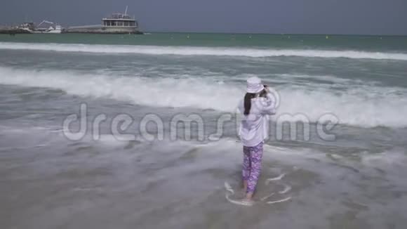 年轻女孩在迪拜海滩上的智能手机上拍摄波斯湾海浪的照片视频的预览图