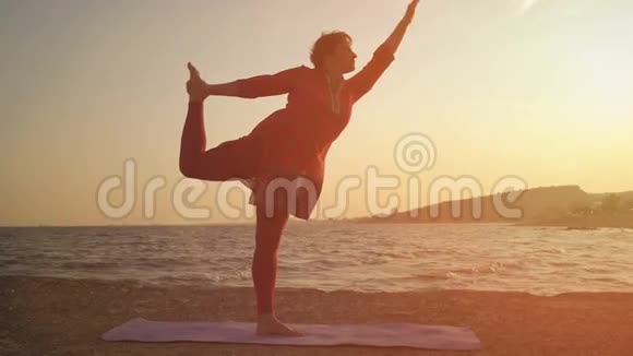 在海滩上日落时瑜伽做瑜伽做体式的女人视频的预览图