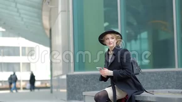 女子玩现代黑色帽子移动宽边黑大衣底部在街上慢动作低角度拍摄视频的预览图