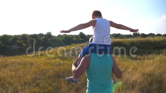 父亲和儿子在阳光明媚的日子在夏天的田野上玩耍小男孩坐在爸爸的肩膀上玩起来视频的预览图