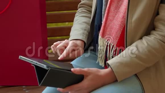 在阳光明媚的天气里坐在长凳上的女孩使用平板电脑并在线订购视频的预览图