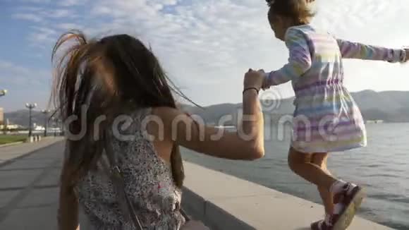 早上女人和一个美丽的小女孩在海滨散步视频的预览图