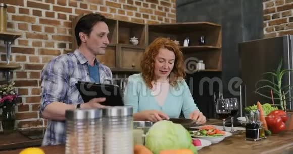 夫妻俩在厨房一起用平板电脑的菜谱做饭男女在家准备食物视频的预览图