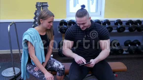 私人教练在健身房的平板电脑上展示年轻女性的运动视频的预览图