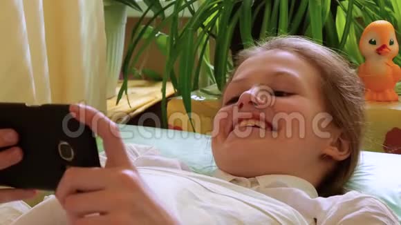 小女孩在智能手机上看视频躺在医院的沙发上笑个不停视频的预览图