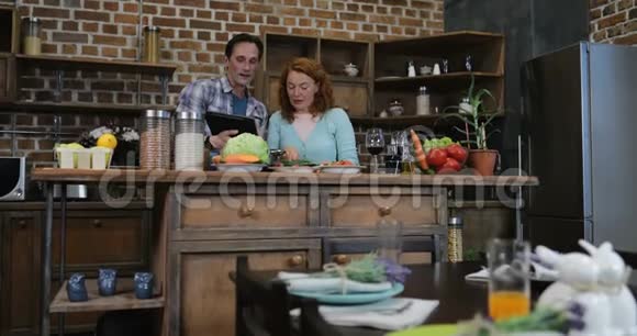 幸福夫妻在厨房用数码平板电脑做饭男女在家一起做饭视频的预览图