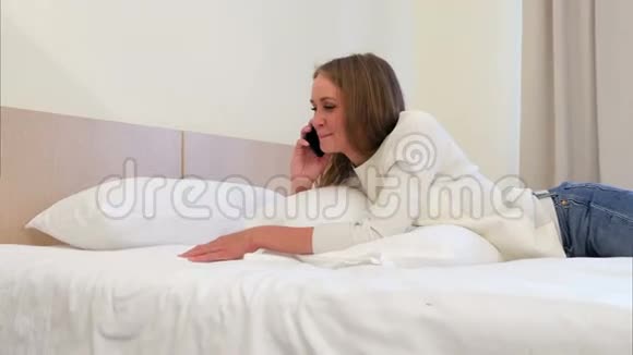 快乐的女人在电话里微笑着躺在酒店的床上聊天视频的预览图