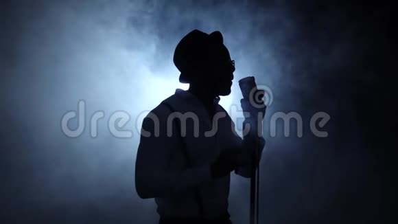 歌手一半在烟雾和白光中翻唱对着麦克风唱歌黑色背景轮廓慢视频的预览图