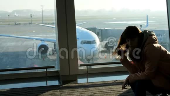 在机场在候机室在一扇窗户的背景下俯瞰着飞机和跑道一个年轻人视频的预览图