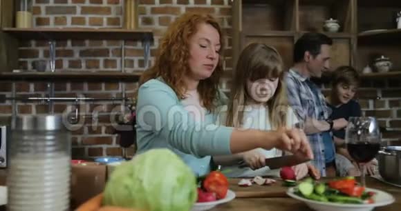 母亲和女儿在父子间用平板电脑切菜幸福的家庭一起做饭视频的预览图