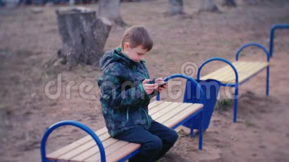 男孩坐在公园里的长凳上用手机玩游戏视频的预览图