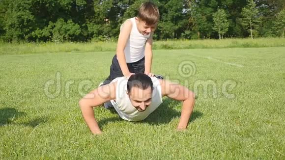 父亲带着儿子从森林里的地上拧下来男孩被训练变得更强壮自然运动上午视频的预览图