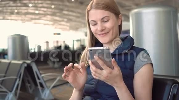美丽迷人的年轻女子在机场使用智能手机和她的朋友聊天微笑视频的预览图