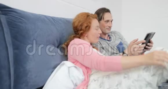 使用数码平板电脑躺在床上的情侣男人和女人在卧室里聊天浏览互联网视频的预览图