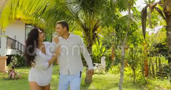 情侣漫步在别墅附近的热带花园里欢乐的男人和女人在户外亲吻度假的情侣视频的预览图