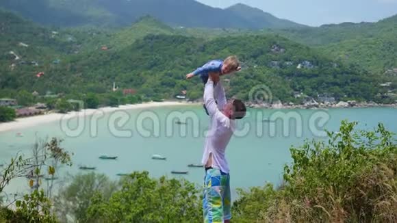 一个带着孩子在山海背景下玩耍的年轻人视频的预览图