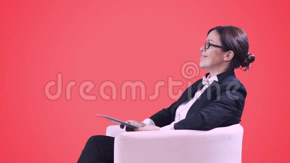 戴眼镜的女商人穿着西装坐在工作室接受采访将有关视频的预览图