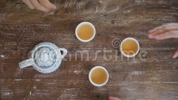 人手捧茶杯从木制的餐桌和饮传统的中国绿茶仪式从上面看视频的预览图