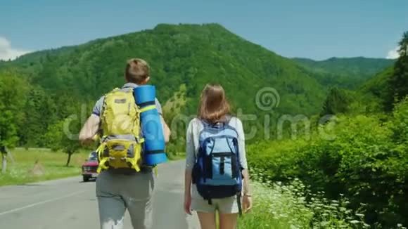 一对年轻的旅游夫妇沿着这条路走到森林覆盖的美丽山脉积极的生活方式和假期视频的预览图
