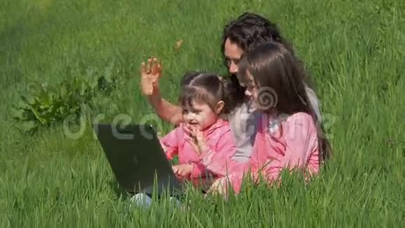 有孩子的女人带着笔记本电脑妈妈和女儿在绿色的草坪上穿粉色衣服的孩子阳光下幸福的家庭视频的预览图