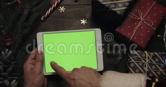 圣诞老人的手在带有绿色屏幕的白色平板电脑上滚动轻敲缩放页面彩色键视频的预览图