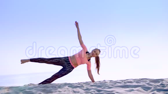 健康年轻的美女做斜腹压肌练习在海滩上日出时做视频的预览图