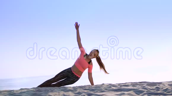 健康年轻的美女做斜腹压肌练习在海滩上日出时做视频的预览图