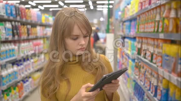 年轻漂亮的女孩在超市购物在平板电脑上寻找有关产品的信息视频的预览图