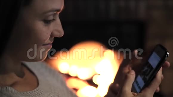 年轻女子坐在壁炉前手里拿着智能手机视频的预览图