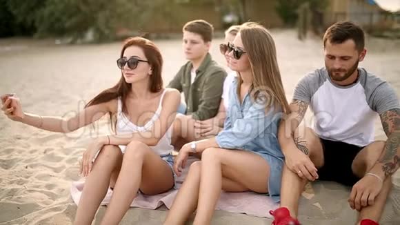 拍摄一群年轻朋友在海滩上自拍男人和女人坐在温暖的沙滩上拍照视频的预览图