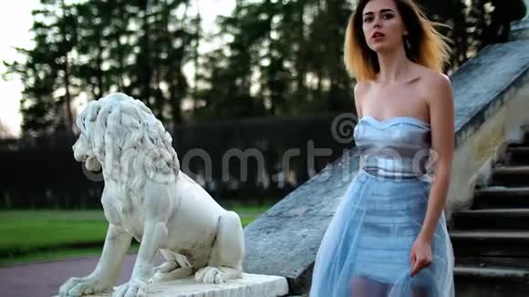 穿着银色和蓝色连衣裙的漂亮女孩站在楼梯上石栏杆靠近狮子雕像摆姿势说话视频的预览图