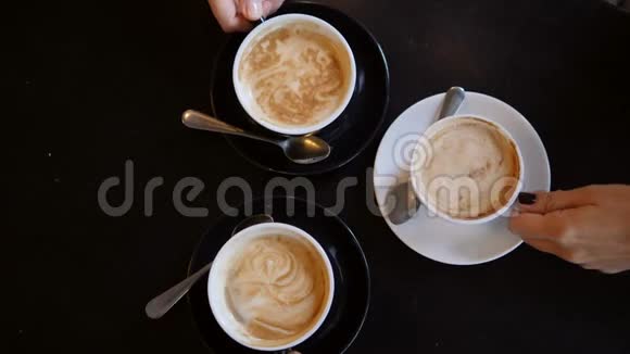 手拿杯子与卡布奇诺咖啡从黑桌在咖啡厅从上面看4K视频的预览图