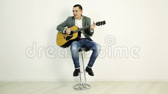 一个穿夹克衫的年轻人坐在酒吧凳子上弹声吉他视频的预览图