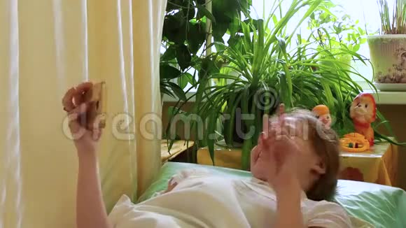 女孩有视频电话少年挥动她的手躺在床上说话微笑视频的预览图