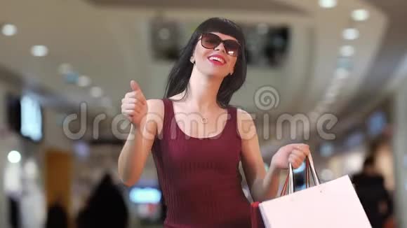 一位身穿勃艮第大衣和眼镜的美丽黑发女子正在商场里跳舞买了新东西慢动作视频的预览图
