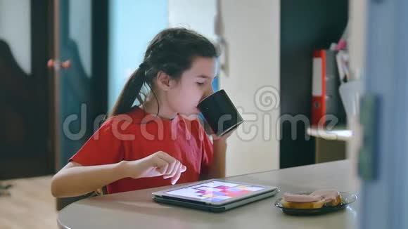 小女孩在玩数字平板电脑吃三明治坐在桌旁玩数字平板电脑的小女孩视频的预览图