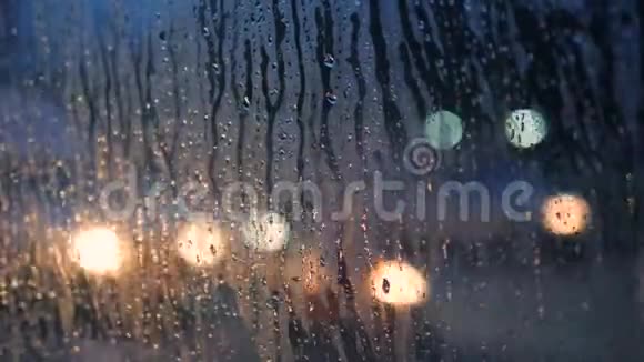 以模糊的夜晚城市汽车灯光为背景在混合车窗玻璃上关闭雨滴4K视频的预览图