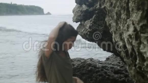 在海边的岩石旁边摆姿势的现代时髦女孩视频的预览图