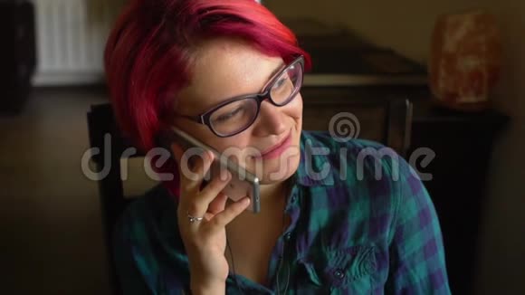 一位漂亮的多彩发女郎戴着时髦眼镜戴着智能手机在咖啡馆里谈笑风生视频的预览图