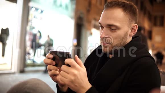 年轻的帅哥晚上在咖啡馆里度过闲暇时光使用带有触摸屏的智能手机视频的预览图