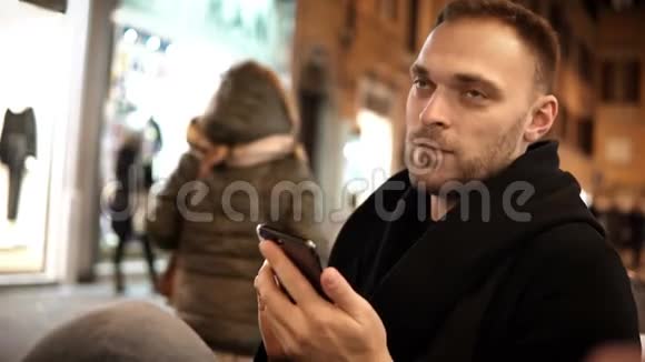 年轻的帅哥晚上坐在咖啡馆里在互联网上使用智能手机一个人花时间视频的预览图