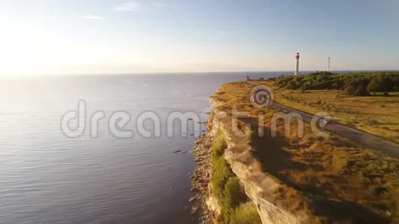 夏季日落时沿海崖驾驶黑色汽车的鸟瞰图在老灯塔的背景下视频的预览图